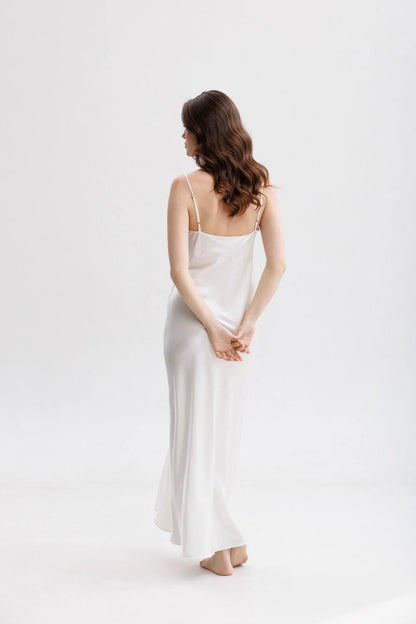 Woman wearing a long silk white slip dress on a spaghetti straps showing the back pose. 
